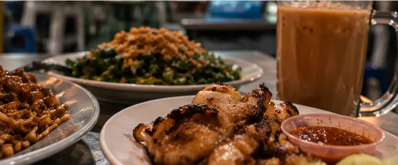 Char kway teow, kai lan, grilled chicken and a glass of kopi on a hawker centre table