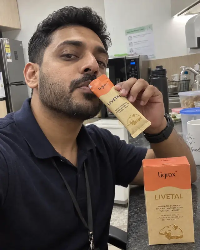 A man drinking a LIVETAL sachet in an office pantry, box on the counter