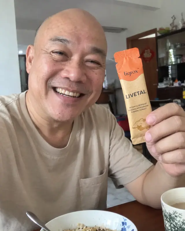 A smiling man holding a LIVETAL sachet at the breakfast table
