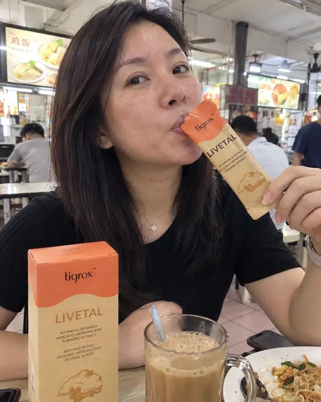 A woman drinking a LIVETAL sachet at a hawker centre next to a kopi