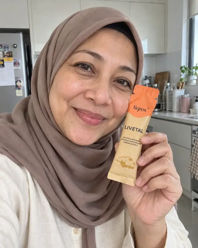 A woman in a hijab holding a LIVETAL sachet in her kitchen