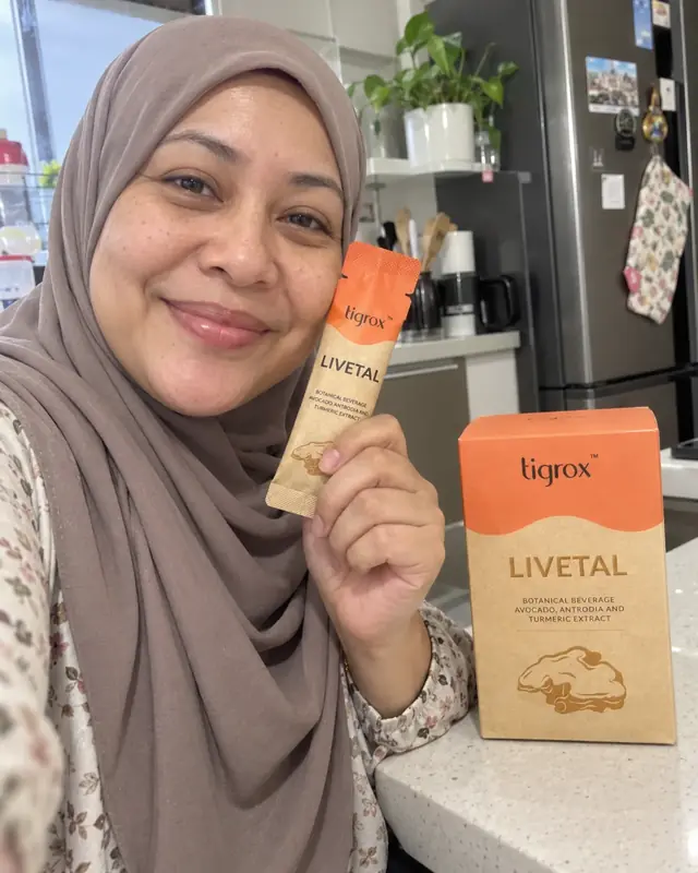 A woman in a hijab holding a LIVETAL sachet and box in her kitchen