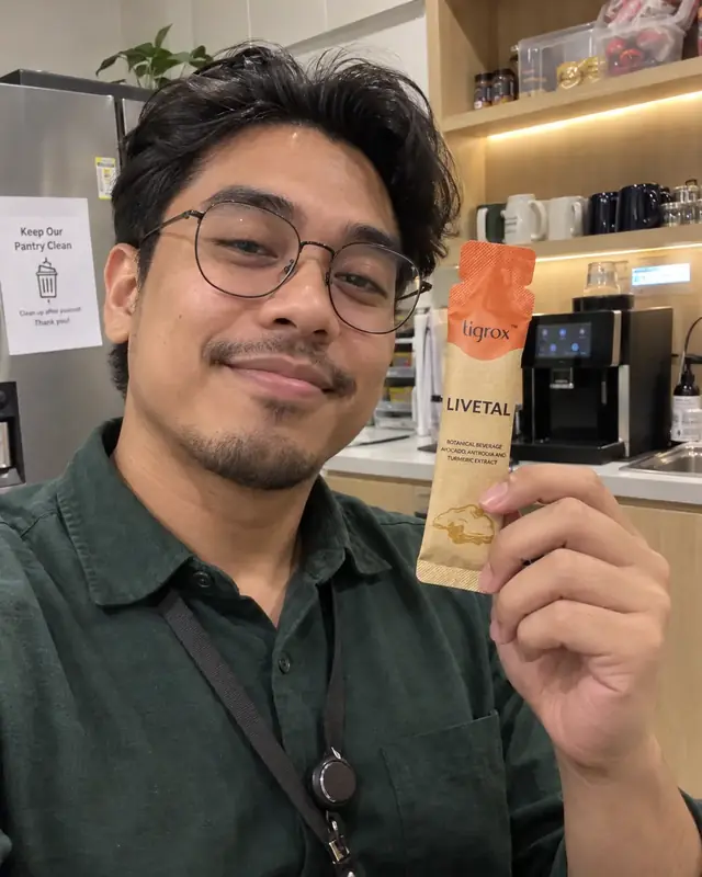 A man with glasses holding a LIVETAL sachet in an office pantry