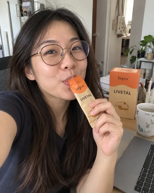 A woman with glasses drinking a LIVETAL sachet at her desk