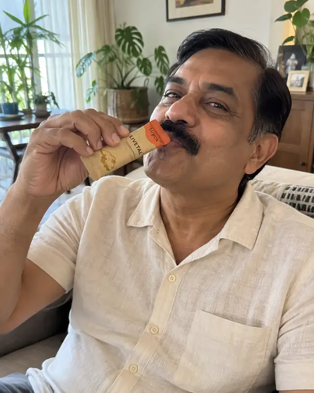 A man drinking a LIVETAL sachet on his sofa